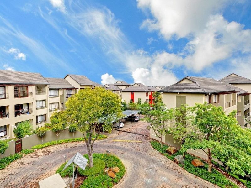 An elevated aerial view of the apartment complex grounds, featuring paved driveways, landscaped gardens, and covered parking areas.