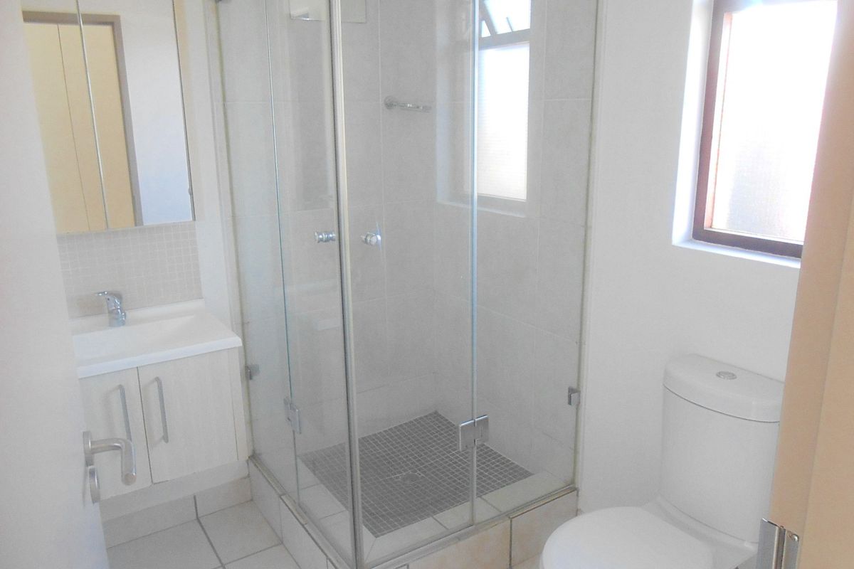 A clean and functional bathroom featuring a glass shower enclosure, vanity cabinet with basin, and a standard toilet.