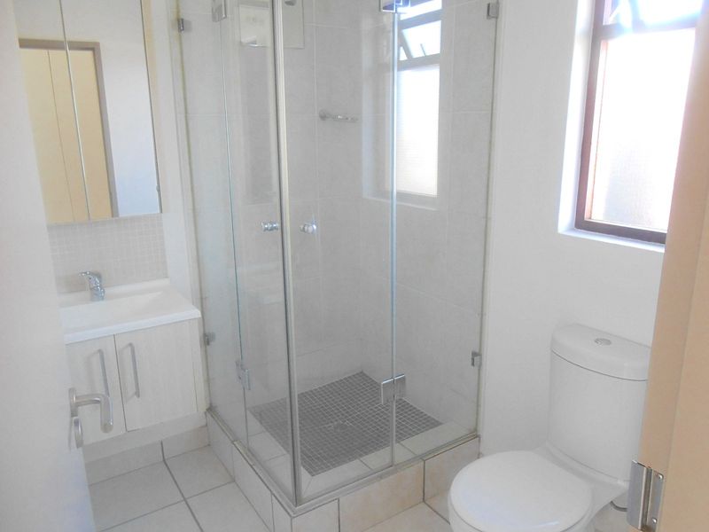 A clean and functional bathroom featuring a glass shower enclosure, vanity cabinet with basin, and a standard toilet.