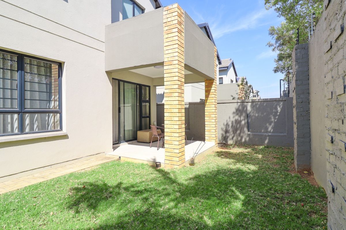 Rear view of the townhouse featuring a covered patio with brick pillars, sliding glass doors, and a private garden area with perimeter walling.