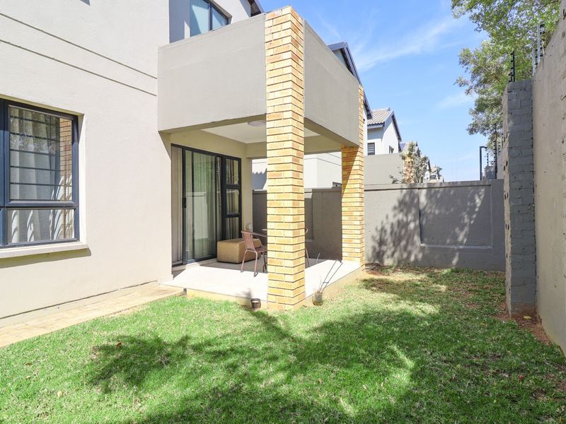 Rear view of the townhouse featuring a covered patio with brick pillars, sliding glass doors, and a private garden area with perimeter walling.