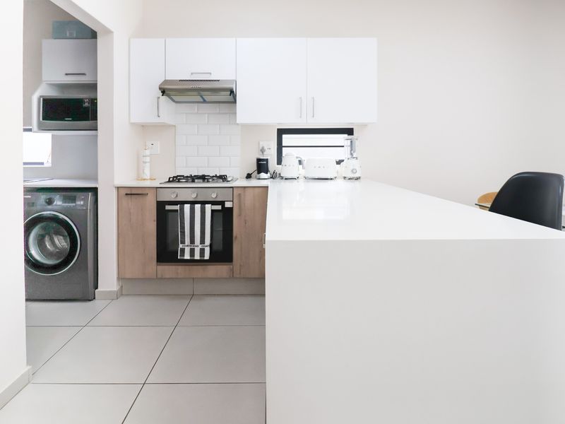 Modern open-plan kitchen featuring a gas hob, built-in oven, extractor fan, subway tile backsplash, and a sleek quartz breakfast bar island.