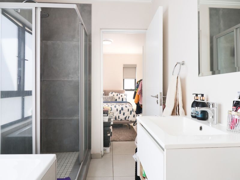Modern bathroom featuring a glass-enclosed shower, sleek vanity with basin, and neutral tiled finishes, with direct access to the adjacent bedroom.