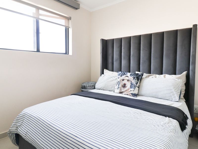 A well-lit bedroom featuring neutral walls, tiled flooring, and a large window with a roller blind.