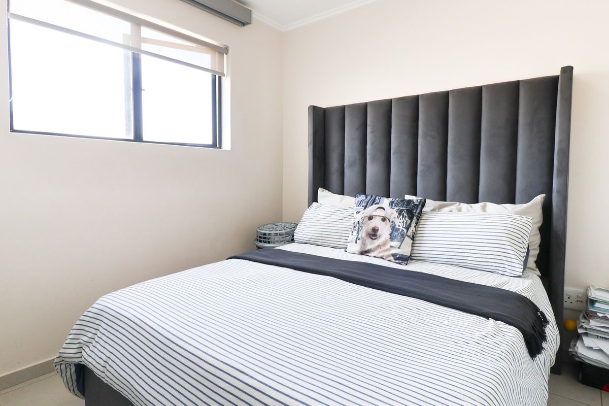 A well-lit bedroom featuring neutral walls, tiled flooring, and a large window with a roller blind.