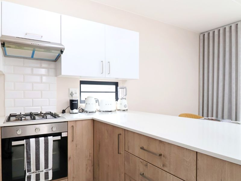 Modern kitchen featuring light wood-finish cabinetry, white quartz countertops, a gas hob, built-in oven, and a classic white subway tile backsplash.