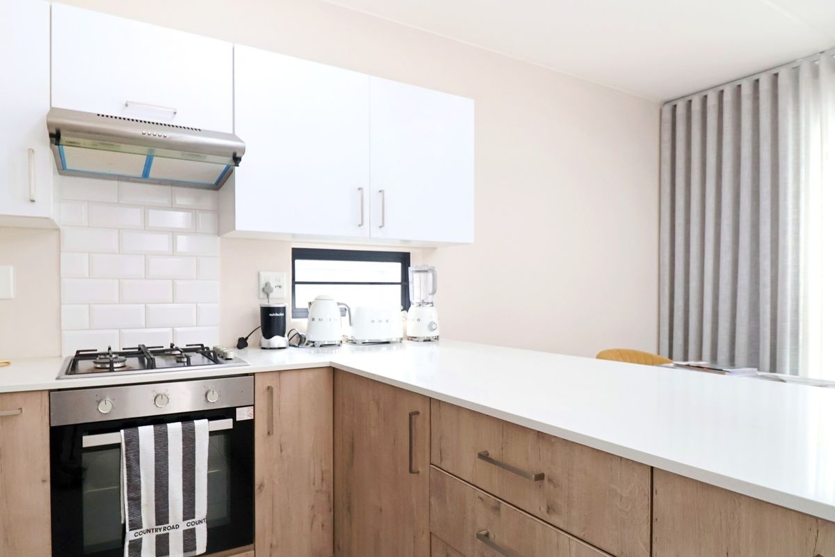 Modern kitchen featuring light wood-finish cabinetry, white quartz countertops, a gas hob, built-in oven, and a classic white subway tile backsplash.