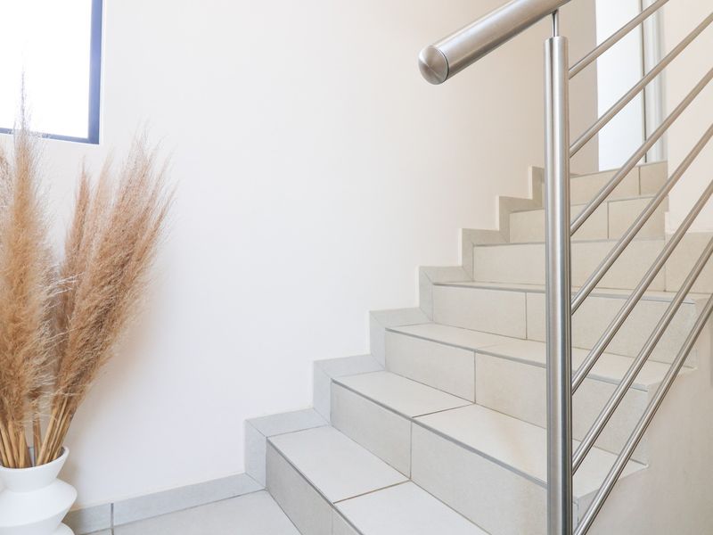 A bright hallway featuring a tiled staircase with a modern stainless steel balustrade and a fixed window.