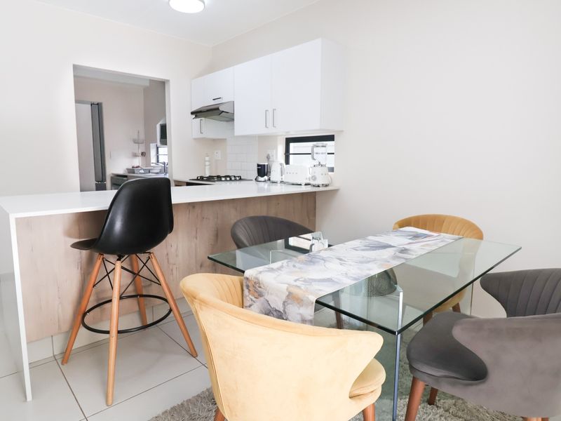 Modern open-plan kitchen and dining area featuring sleek white cabinetry, a breakfast bar, and neutral tiled flooring.