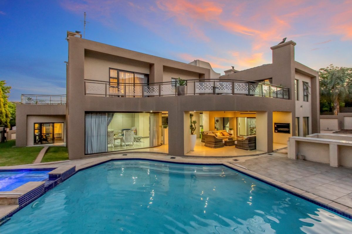 Rear exterior view featuring a swimming pool, spacious covered patio with built-in braai, and an upper-level balcony overlooking the garden.