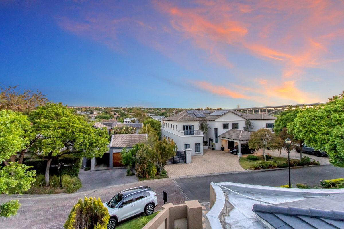 Elevated aerial view of a well-maintained residential property featuring a paved driveway, tiled roof, solar panels, and established garden landscaping.