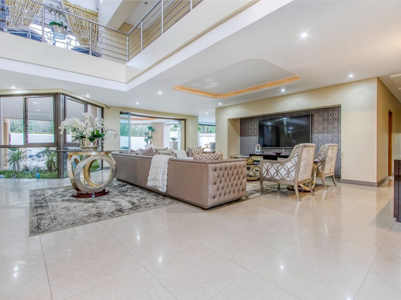 Spacious double-volume living room featuring tiled floors, a modern media wall, and a mezzanine level with a stainless steel balustrade.