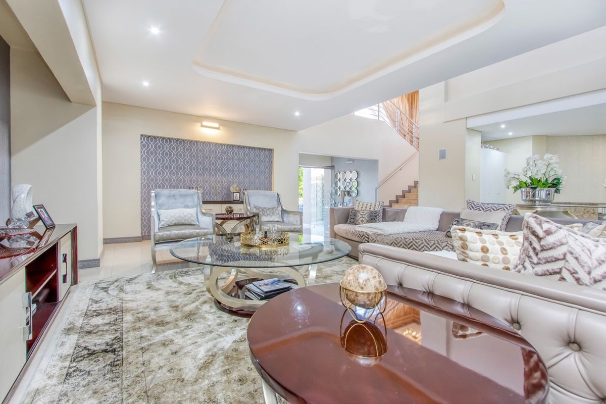 Spacious living room featuring a recessed ceiling with downlights, tiled flooring, and an elegant feature wall, leading to an open staircase.
