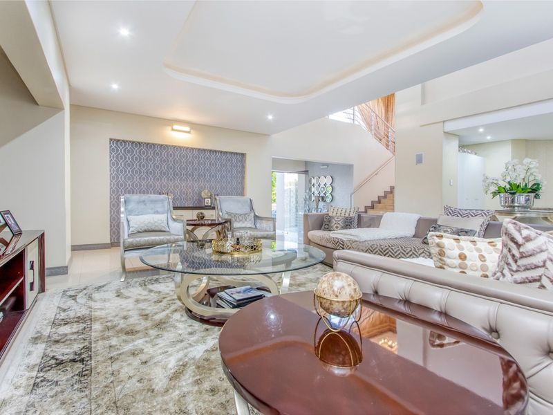 Spacious living room featuring a recessed ceiling with downlights, tiled flooring, and an elegant feature wall, leading to an open staircase.