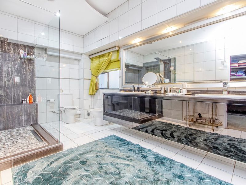 Spacious modern bathroom featuring a double vanity, large wall mirror, walk-in shower with glass screen, wall-mounted toilet, and bidet with tiled finishes.