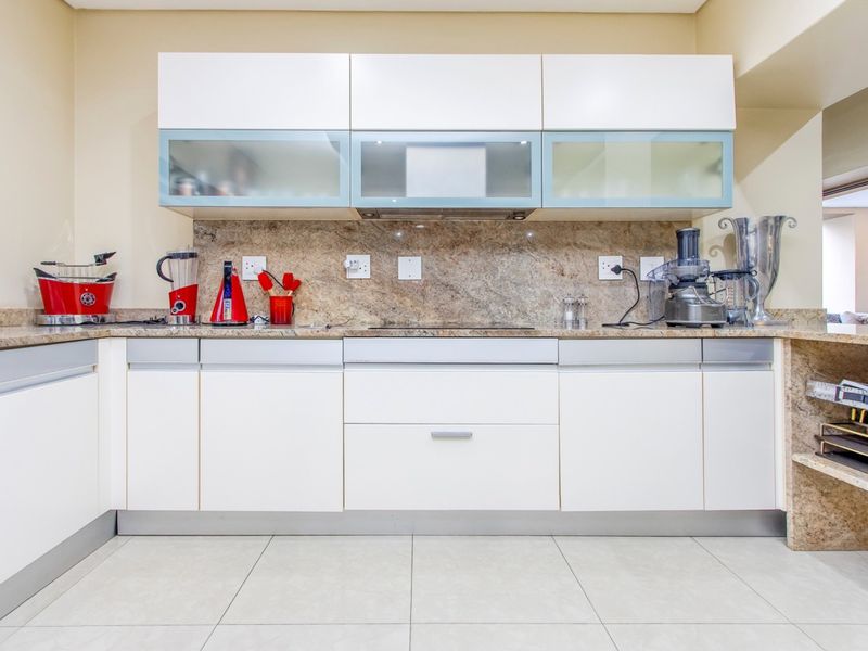 Modern kitchen featuring white cabinetry, granite countertops, glass-front upper cabinets, and ceramic floor tiles, providing a clean and functional workspace.