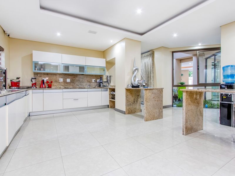 Modern kitchen featuring sleek white cabinetry, stone countertops, tiled flooring, and recessed lighting, with an open layout and direct access to an outdoor area.