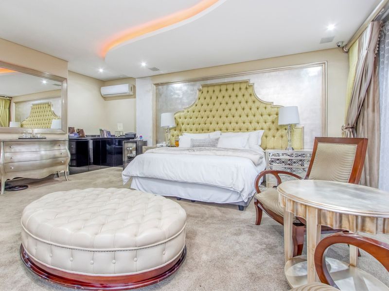 Spacious bedroom featuring a custom tufted headboard, recessed ceiling lighting with cove accents, and a wall-mounted air conditioning unit.