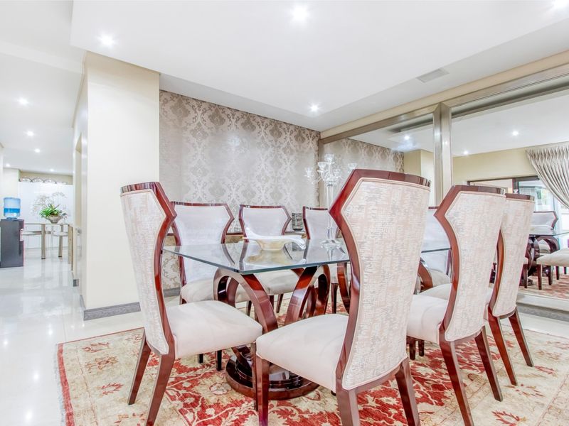 A formal dining room featuring polished porcelain floor tiles, recessed downlighting, and a large decorative mirrored wall panel.
