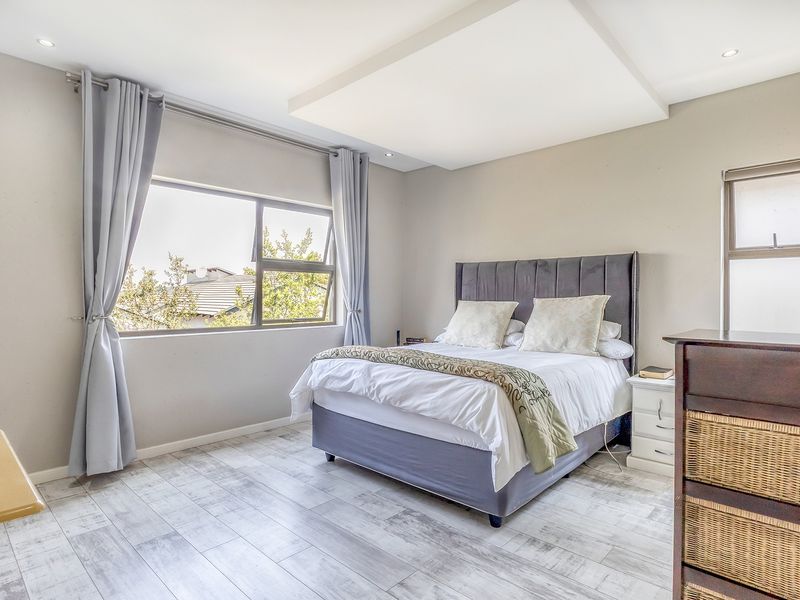 A well-maintained bedroom featuring wood-look tile flooring, a recessed ceiling with downlights, and large windows providing natural light.