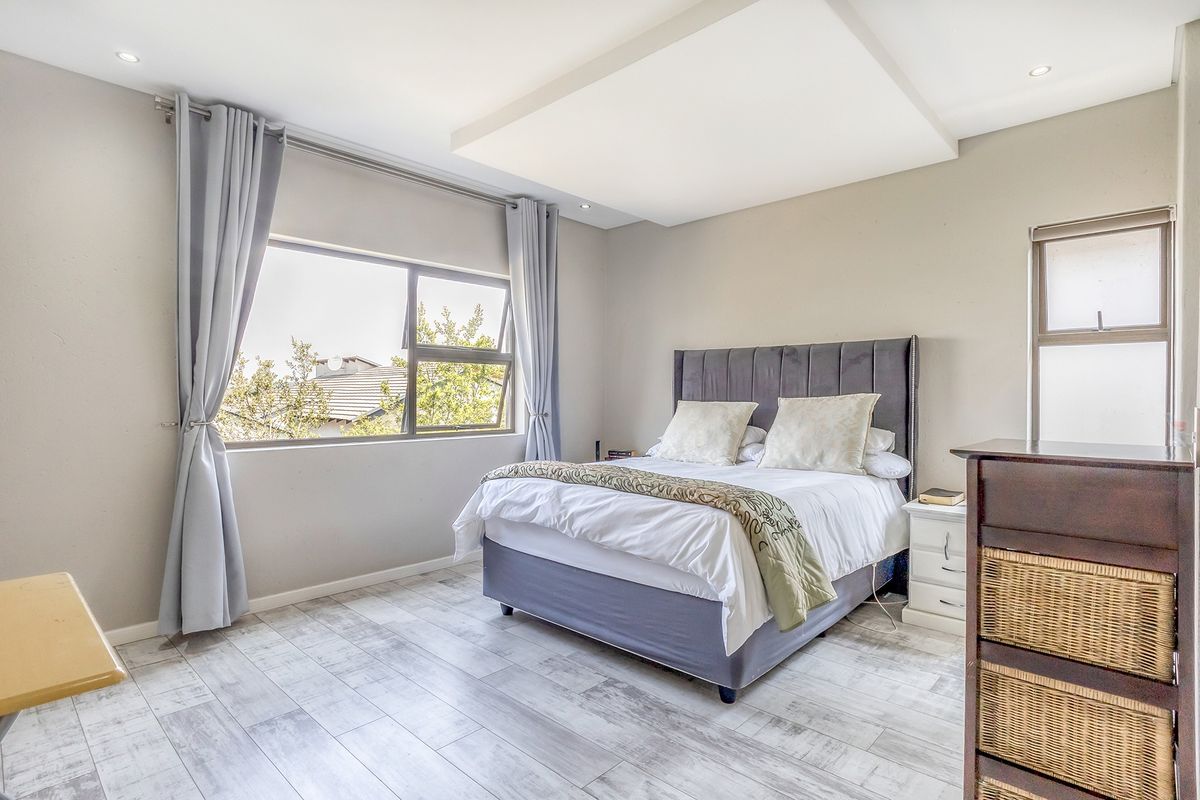 A well-maintained bedroom featuring wood-look tile flooring, a recessed ceiling with downlights, and large windows providing natural light.