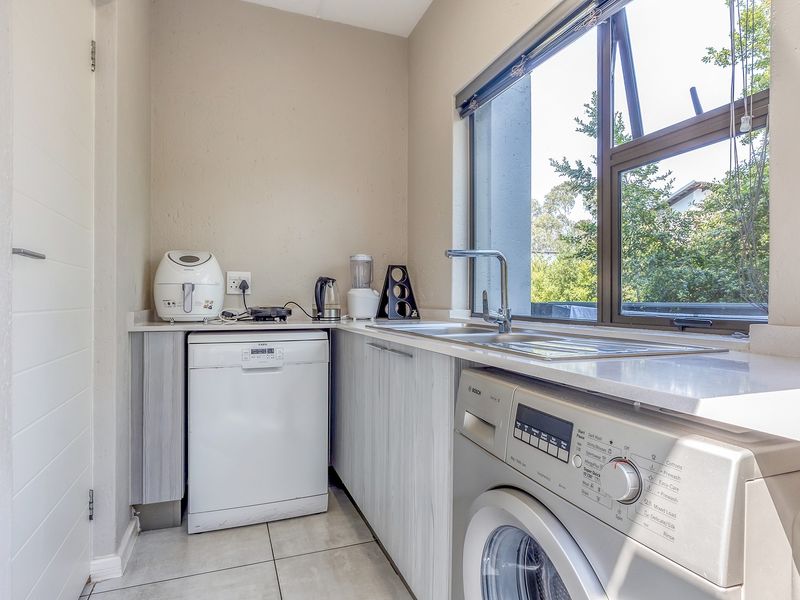 A functional laundry room featuring built-in cabinetry, a stainless steel sink, and tiled flooring, providing a clean and organized utility space.
