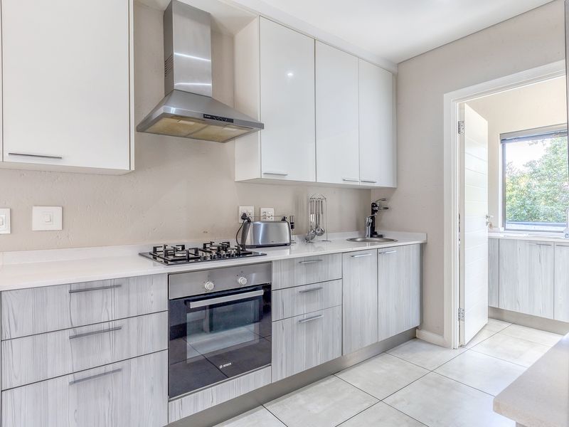 Modern kitchen featuring white gloss upper cabinets, wood-grain lower cabinetry, stone countertops, gas hob, built-in oven, and stainless steel extractor fan.