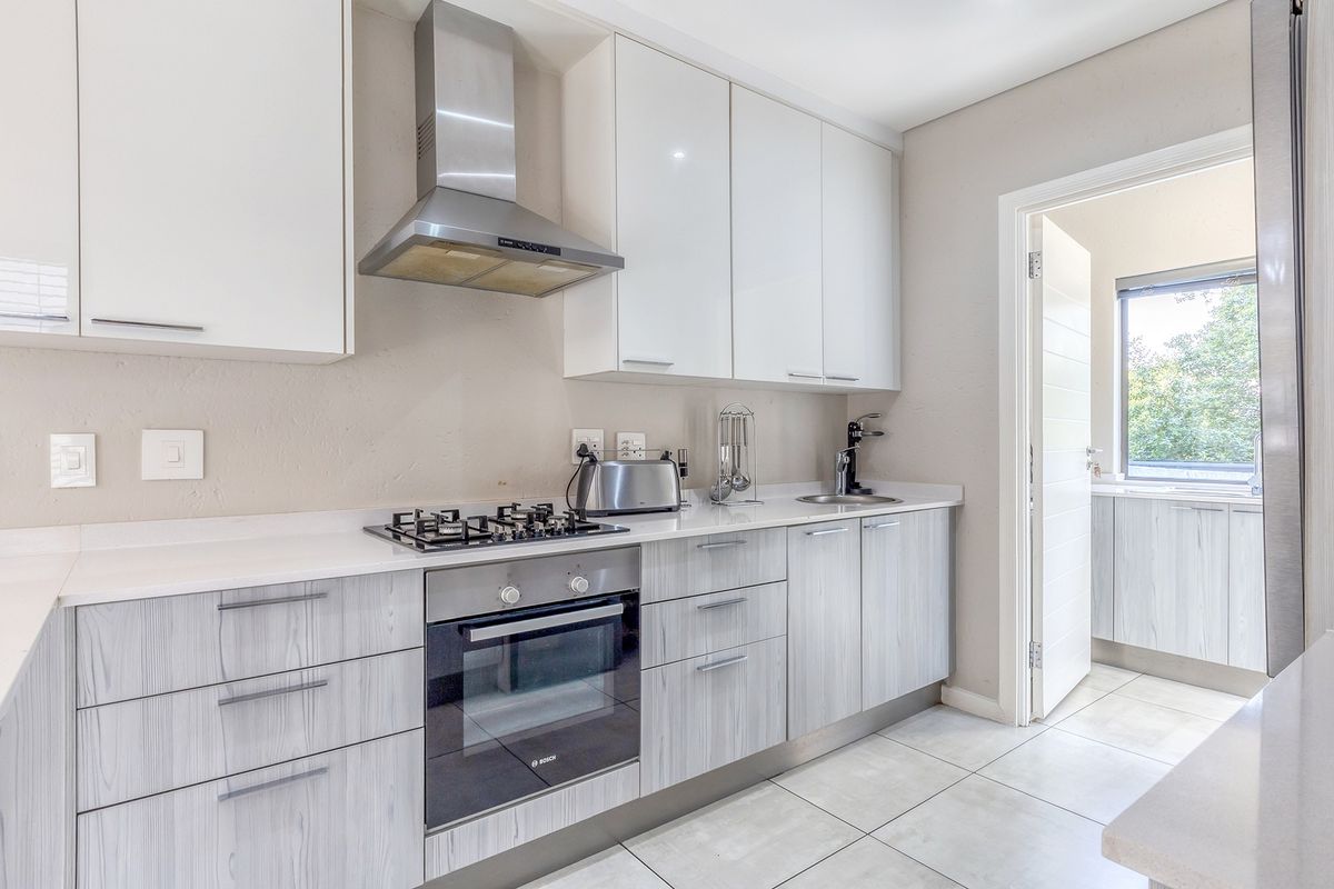 Modern kitchen featuring white gloss upper cabinets, wood-grain lower cabinetry, stone countertops, gas hob, built-in oven, and stainless steel extractor fan.