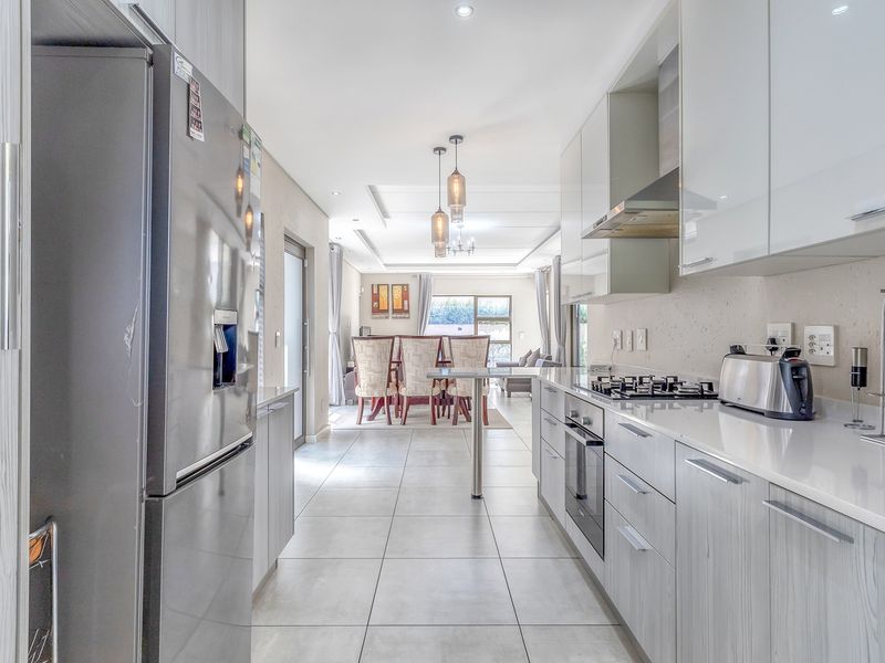 Modern open-plan kitchen featuring sleek gloss cabinetry, stone countertops, and integrated appliances, flowing seamlessly into the dining and living area.