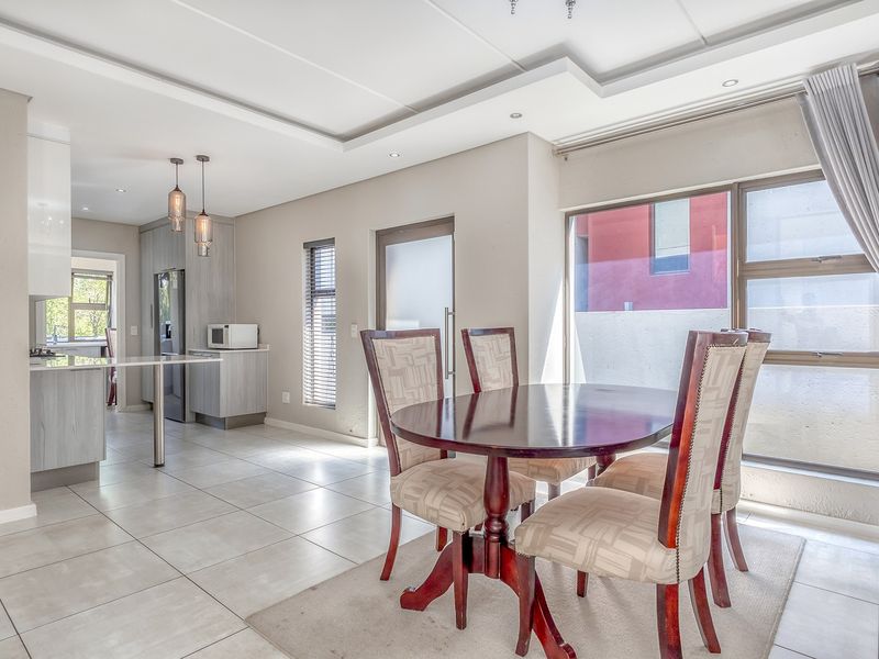 Bright open-plan living and dining area featuring modern tiled floors, a coffered ceiling with recessed lighting, and a sleek, contemporary kitchen with island.