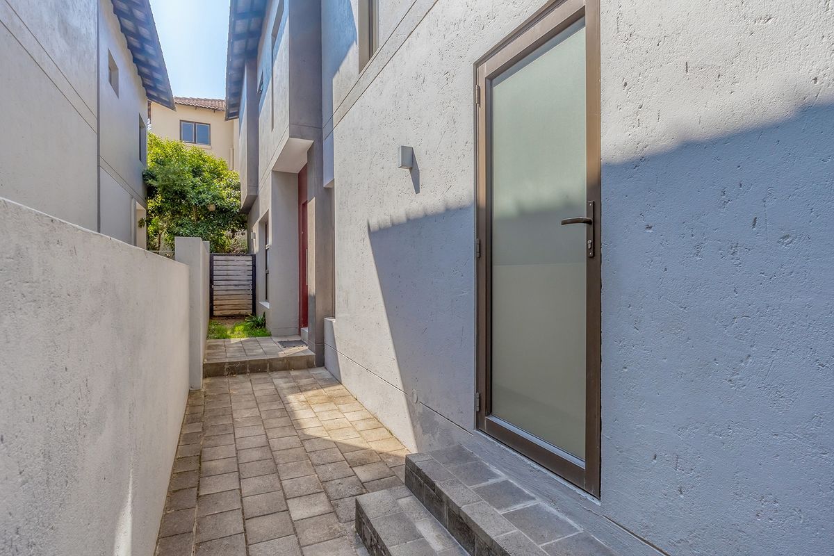 A paved side walkway leading to a rear entrance with a frosted glass door and exterior wall lighting.