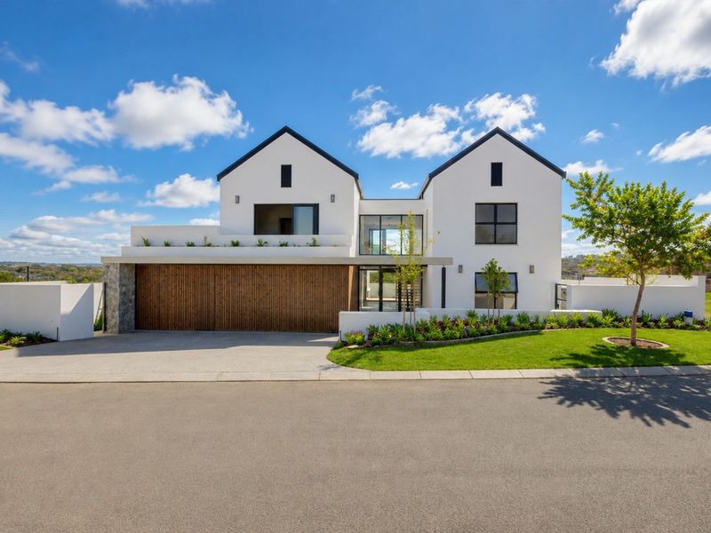 Modern double-story residence featuring a striking white facade, timber garage door, stone accents, and a well-manicured front garden.