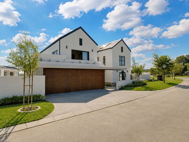 Modern architectural home featuring a timber garage door, clean white plastered facade, and well-maintained landscaped garden in a quiet residential setting.