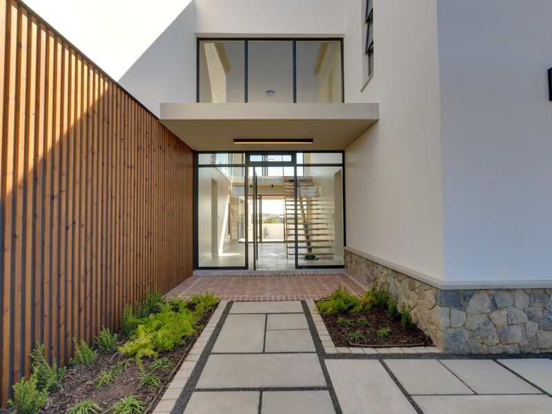 Modern front entrance featuring a combination of timber slat cladding, stone masonry, and a paved walkway leading to a glass-fronted foyer.