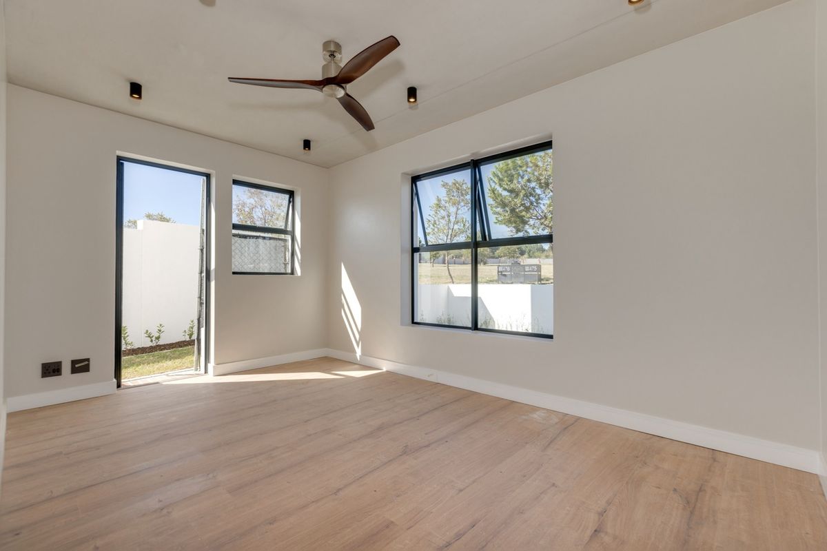 A bright, modern, empty bedroom featuring light wood-look laminate flooring, a ceiling fan, and large black-framed windows providing ample natural light.