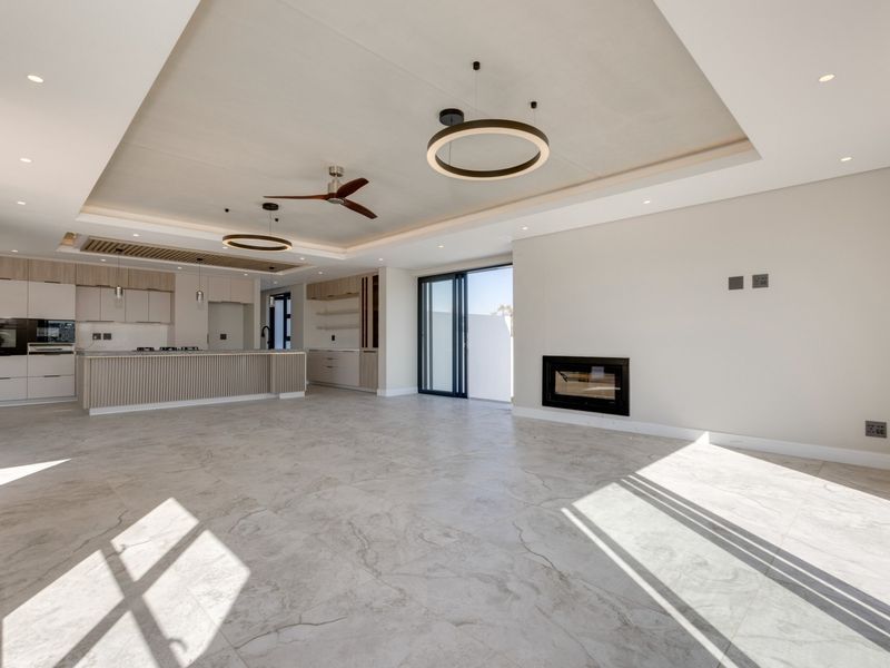 Spacious open-plan living area featuring a modern kitchen with island, built-in fireplace, recessed ceiling details, and large sliding doors leading to the outdoors.