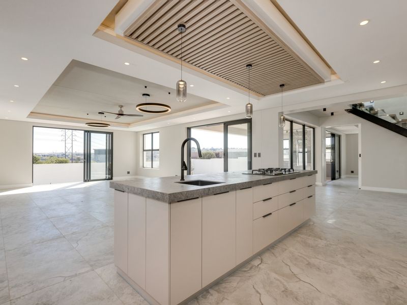 Modern open-plan living and kitchen area featuring a large island with stone countertop, gas cooktop, and a striking slatted timber ceiling detail.