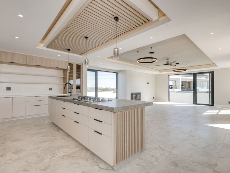 Spacious open-plan living and kitchen area featuring a modern island with gas hob, custom slatted ceiling details, built-in fireplace, and large sliding glass doors.