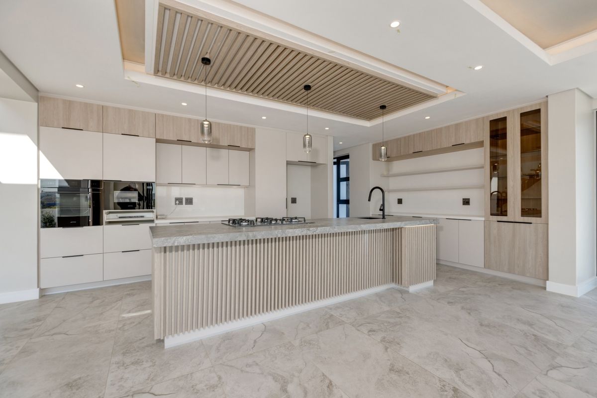 Modern, high-end kitchen featuring a large island with stone countertops, integrated appliances, custom slatted ceiling detail, and premium cabinetry finishes.
