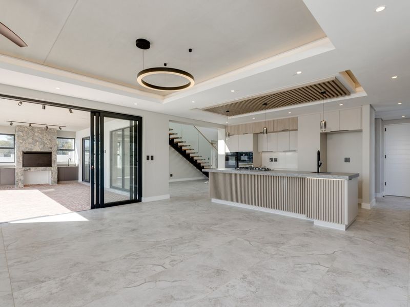 Modern open-plan living area featuring a sleek kitchen with island, stone fireplace, and seamless flow to the outdoor patio through large sliding glass doors.
