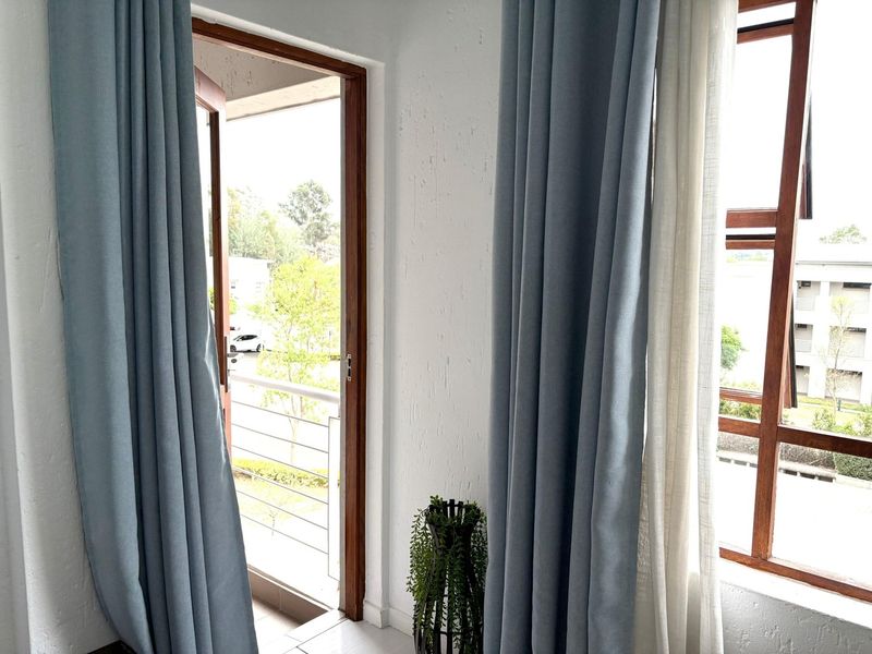 A bright living area featuring timber-framed windows and a door providing direct access to an outdoor balcony.