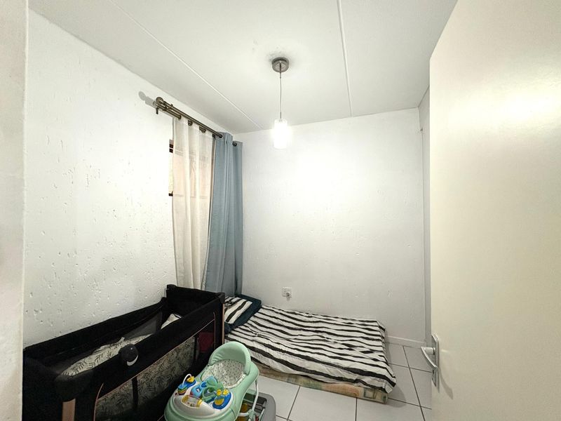 A compact bedroom featuring tiled flooring, a central pendant light, and textured wall finishes.