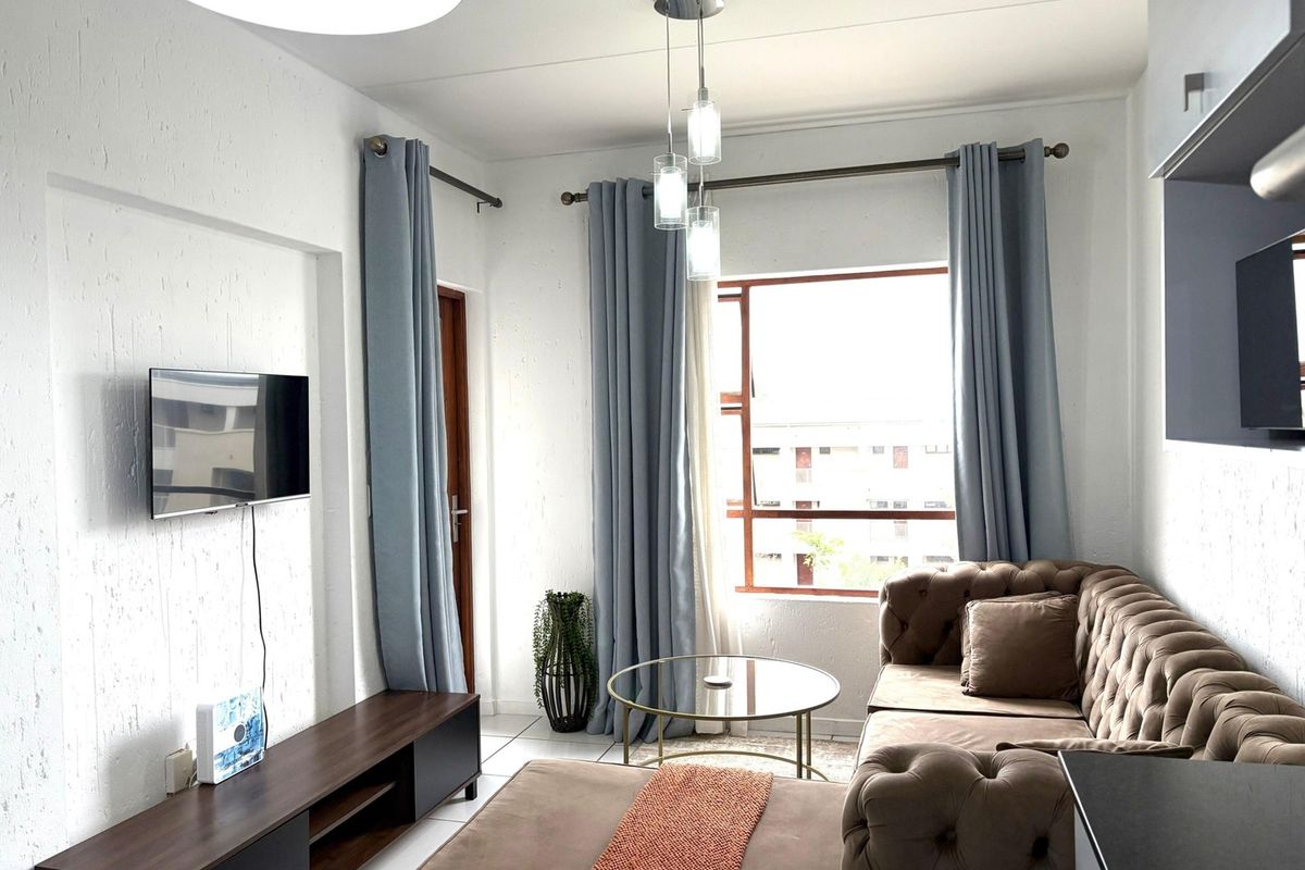 A bright and well-maintained living room featuring tiled flooring, textured walls, and large windows that provide ample natural light.