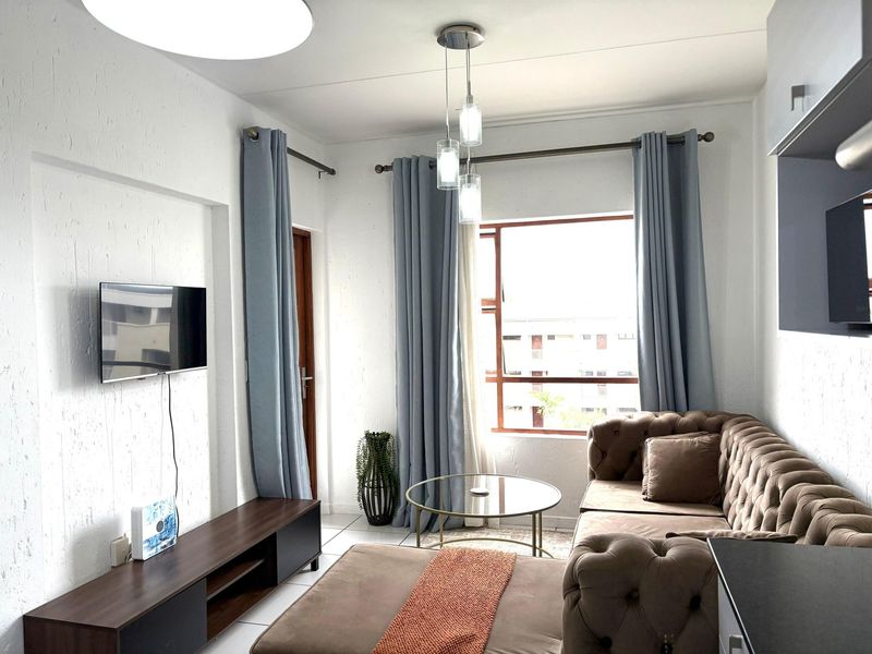 A bright and well-maintained living room featuring tiled flooring, textured walls, and large windows that provide ample natural light.