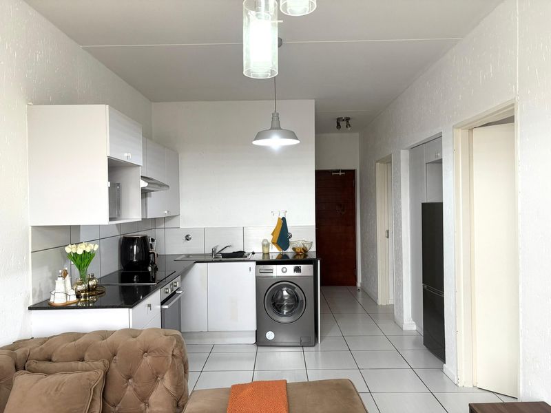 Open-plan kitchen featuring modern white cabinetry, black granite countertops, integrated appliances, and tiled flooring, seamlessly connecting to the living area.