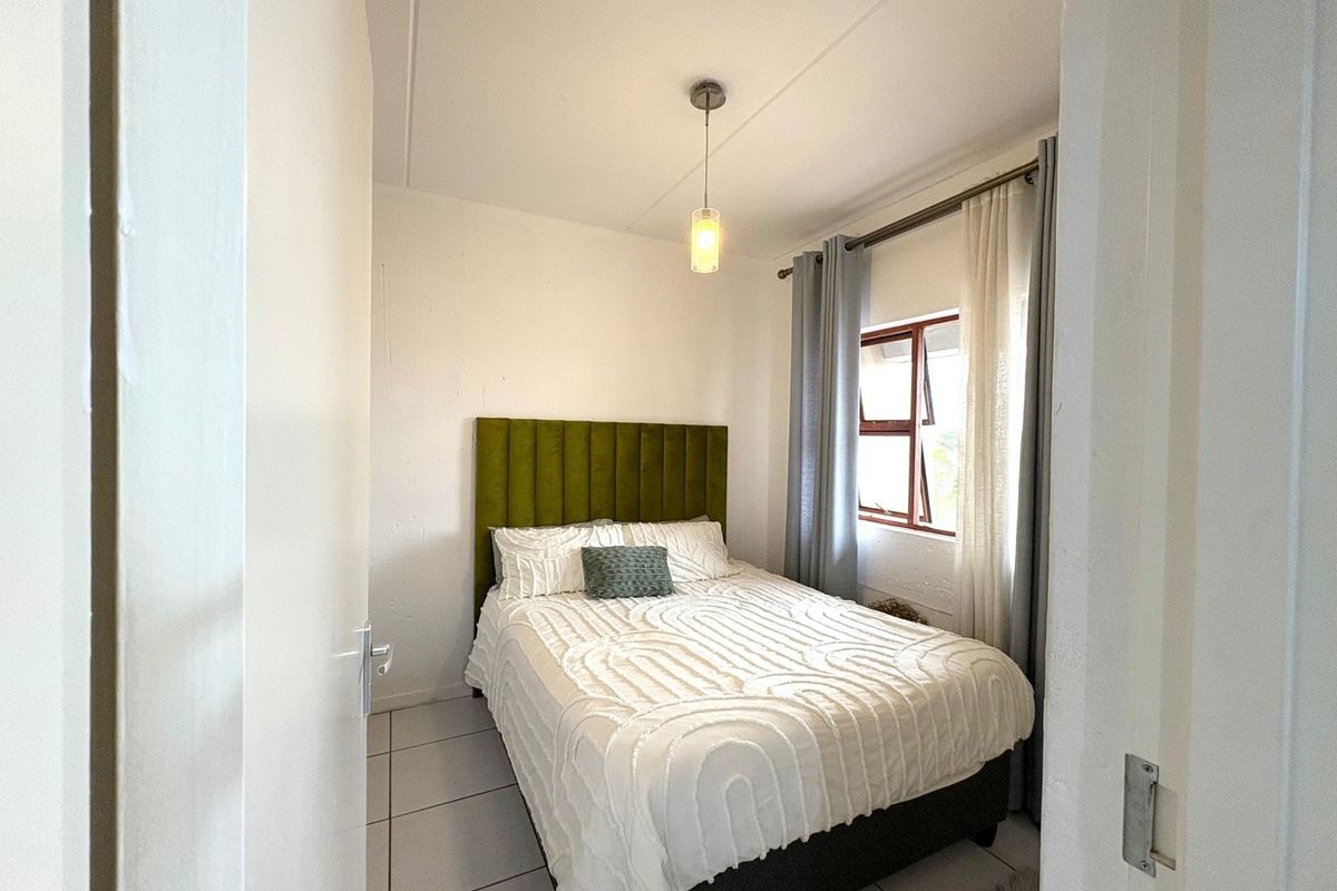 A compact bedroom featuring tiled flooring, a central pendant light, and a top-hung window with curtain tracks.