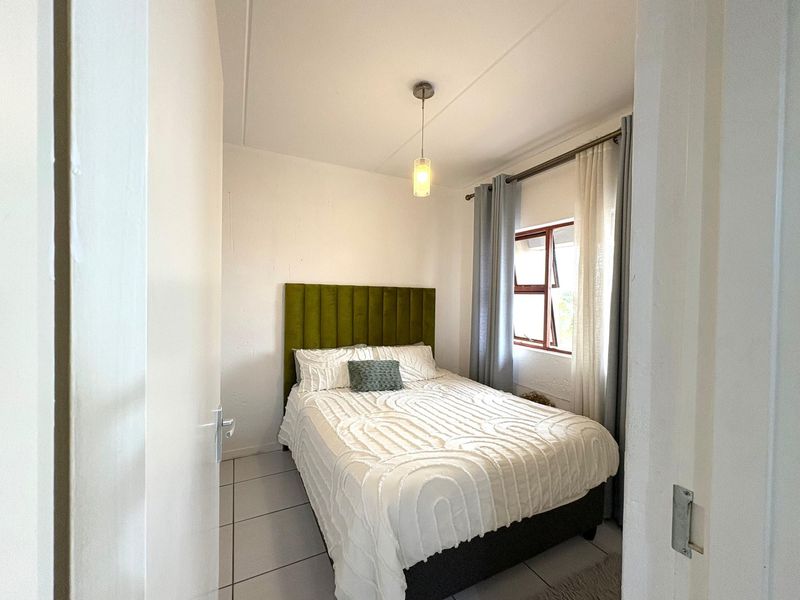A compact bedroom featuring tiled flooring, a central pendant light, and a top-hung window with curtain tracks.