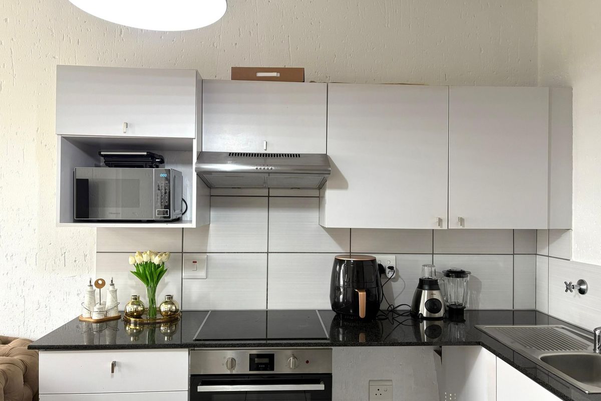 A functional kitchen featuring white cabinetry, a dark granite countertop, built-in oven, electric hob, and a stainless steel extractor fan.