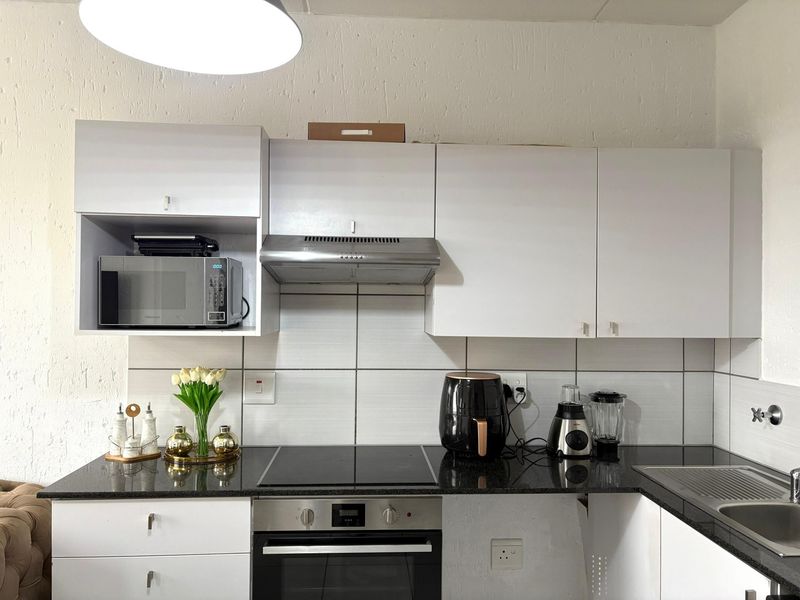 A functional kitchen featuring white cabinetry, a dark granite countertop, built-in oven, electric hob, and a stainless steel extractor fan.