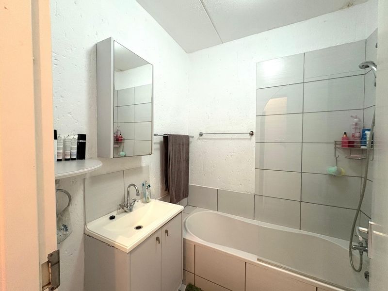 A functional bathroom featuring a vanity with basin, medicine cabinet, and a combined bathtub and shower unit with tiled surround.